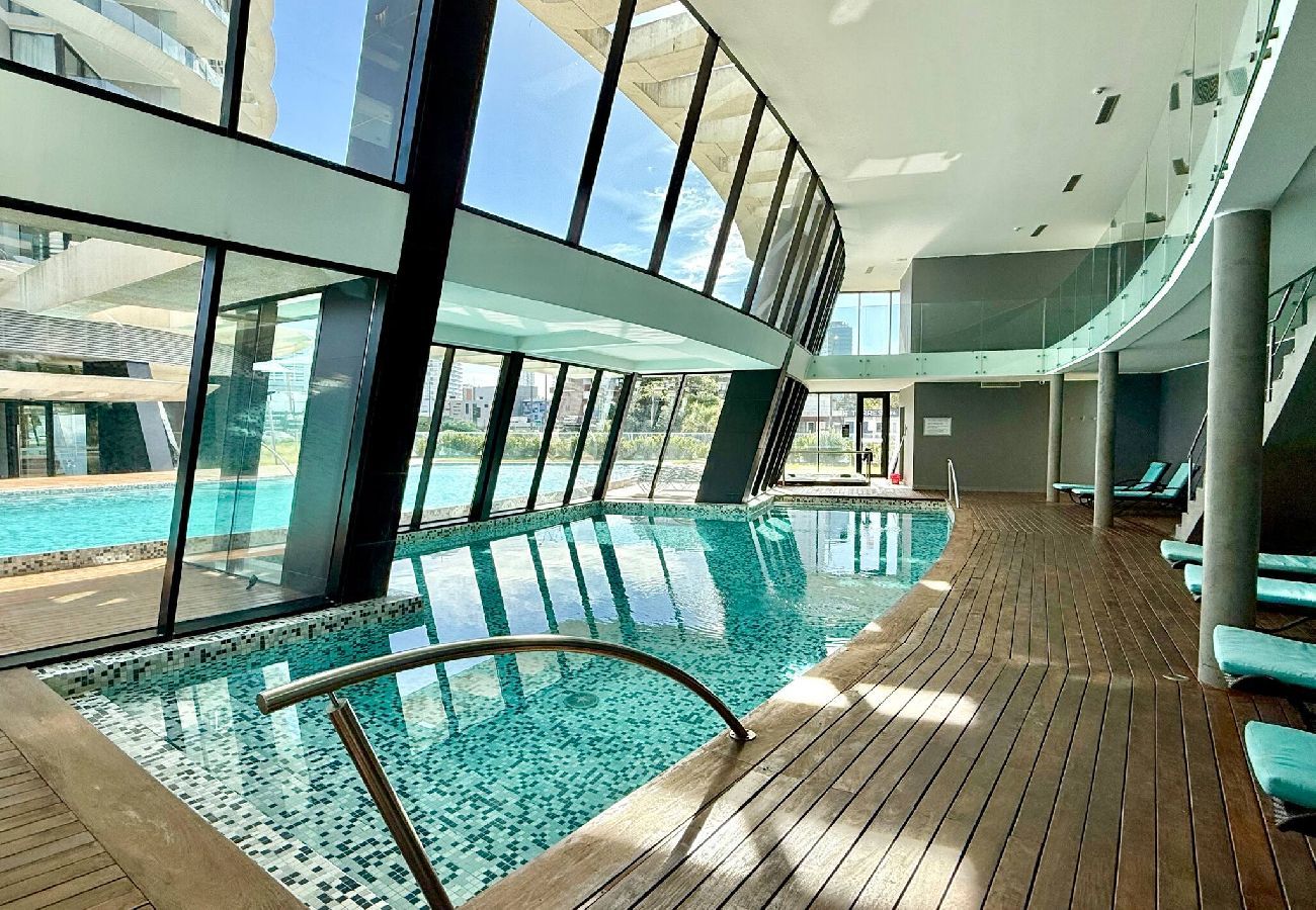 Piscina interior climatizada con ventanales y área de descanso