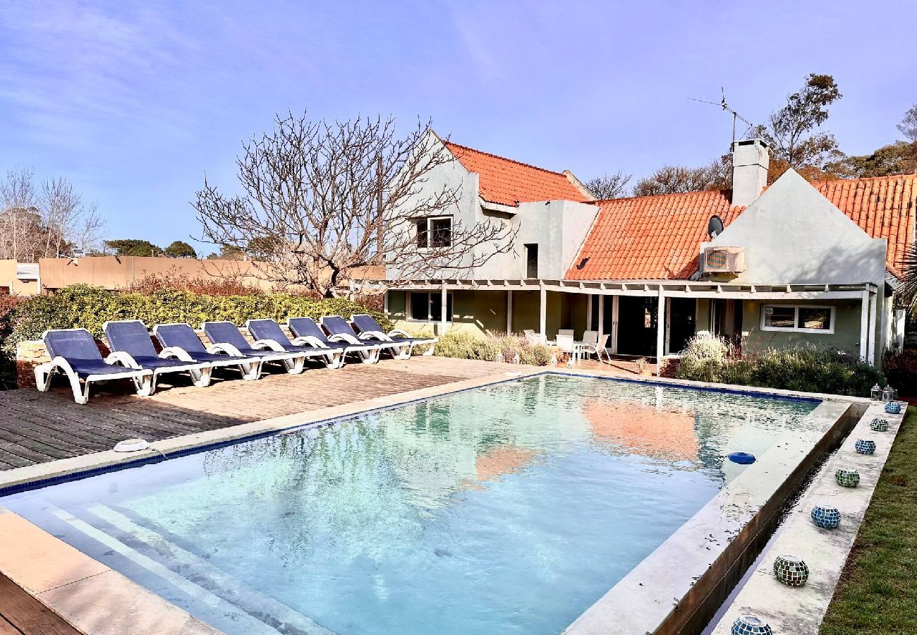 Piscina ampla estilo clube com espreguiçadeiras e casa mediterrânea